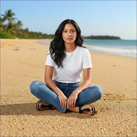Woman sitting on the beach wearing a white t-shirt, blue jeans, and Birkenstock Gizeh flip-flops.