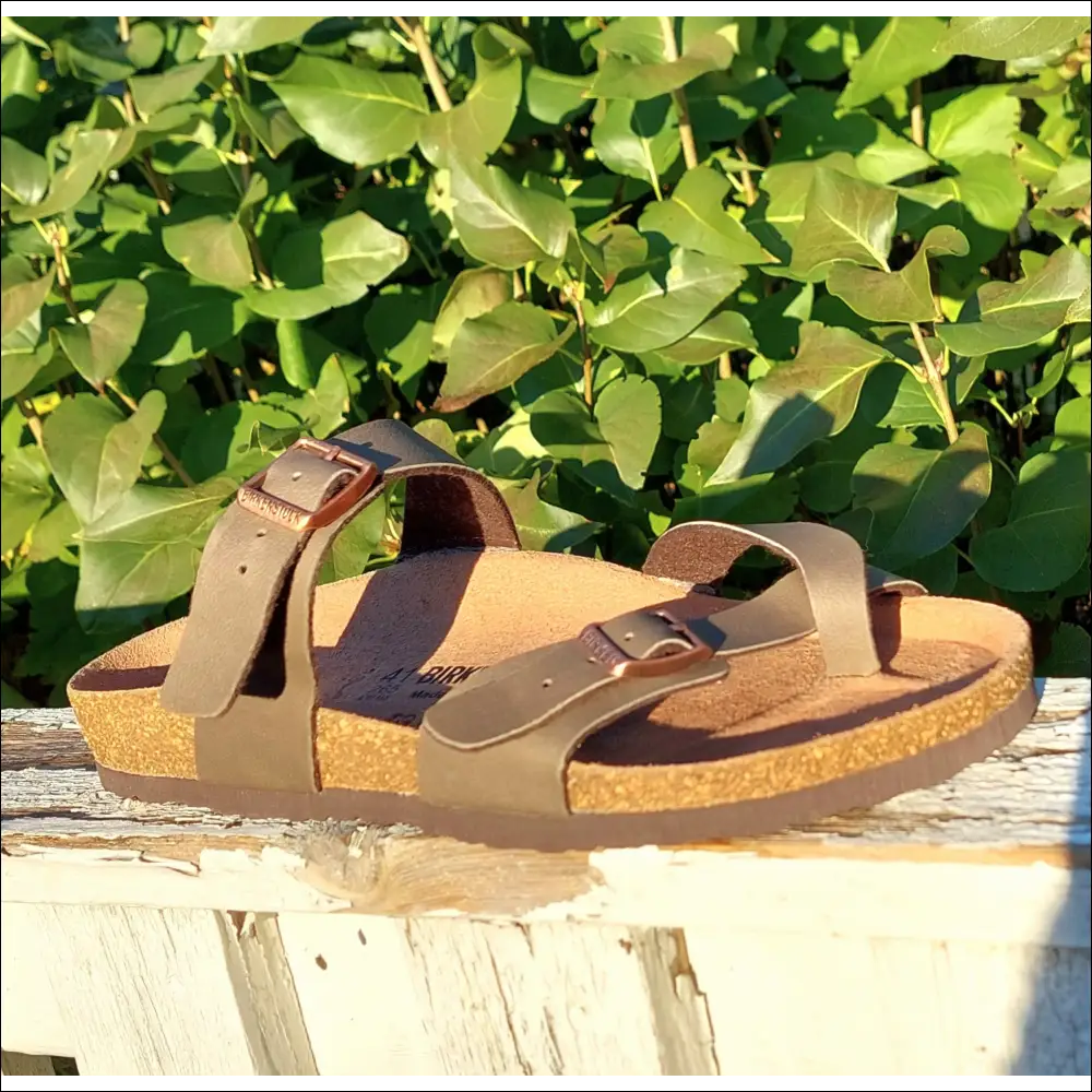 Birkenstock Mayari sandals in Stone Birko-Flor style resting on a wooden surface with green foliage in the background.