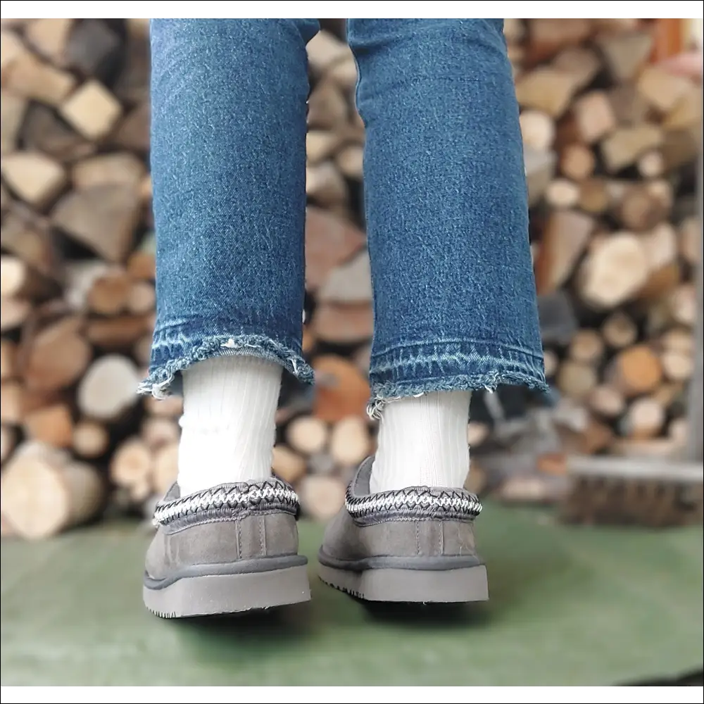 Ugg Tasman II Slipper Mole worn with jeans and white socks, showcasing the stylish design against a wooden backdrop.